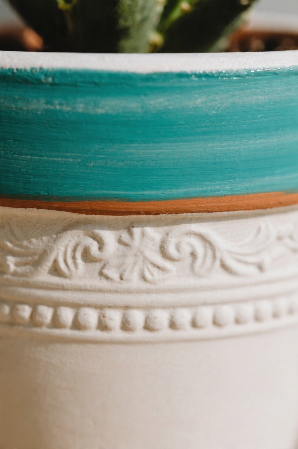A close-up of the rim of a painted flower pot detailed with a contrasting color band and a subtle raised relief trim The