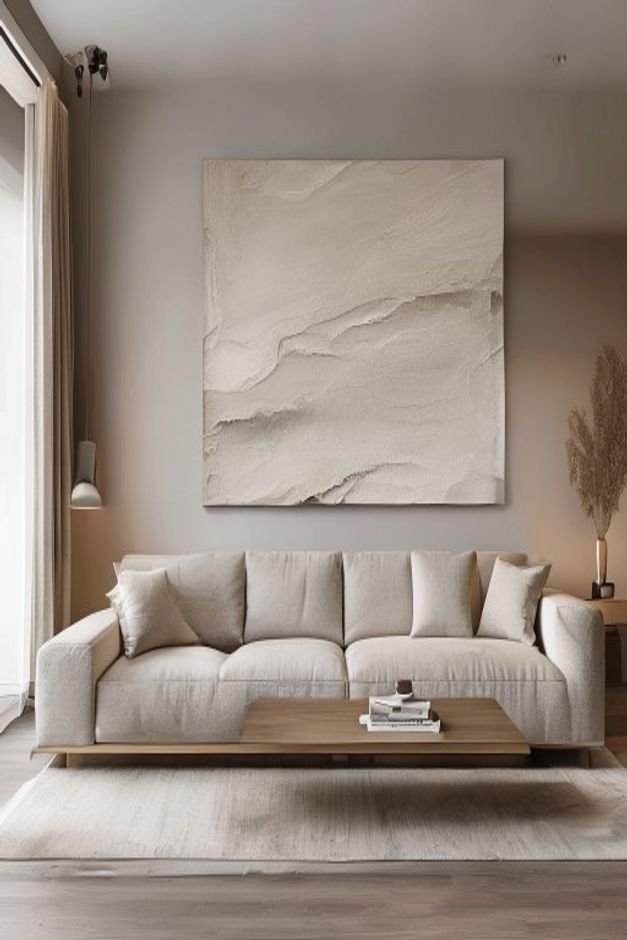 A contemporary living room featuring a long low-slung sofa in a neutral tone Above it a single oversized piece of abstra