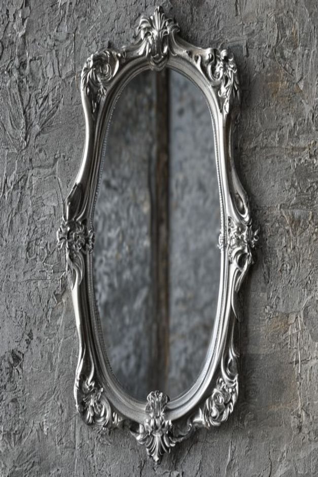 A close-up shot of a mirror with a distinctive intricately carved silver frame hung on a textured gray wall The details